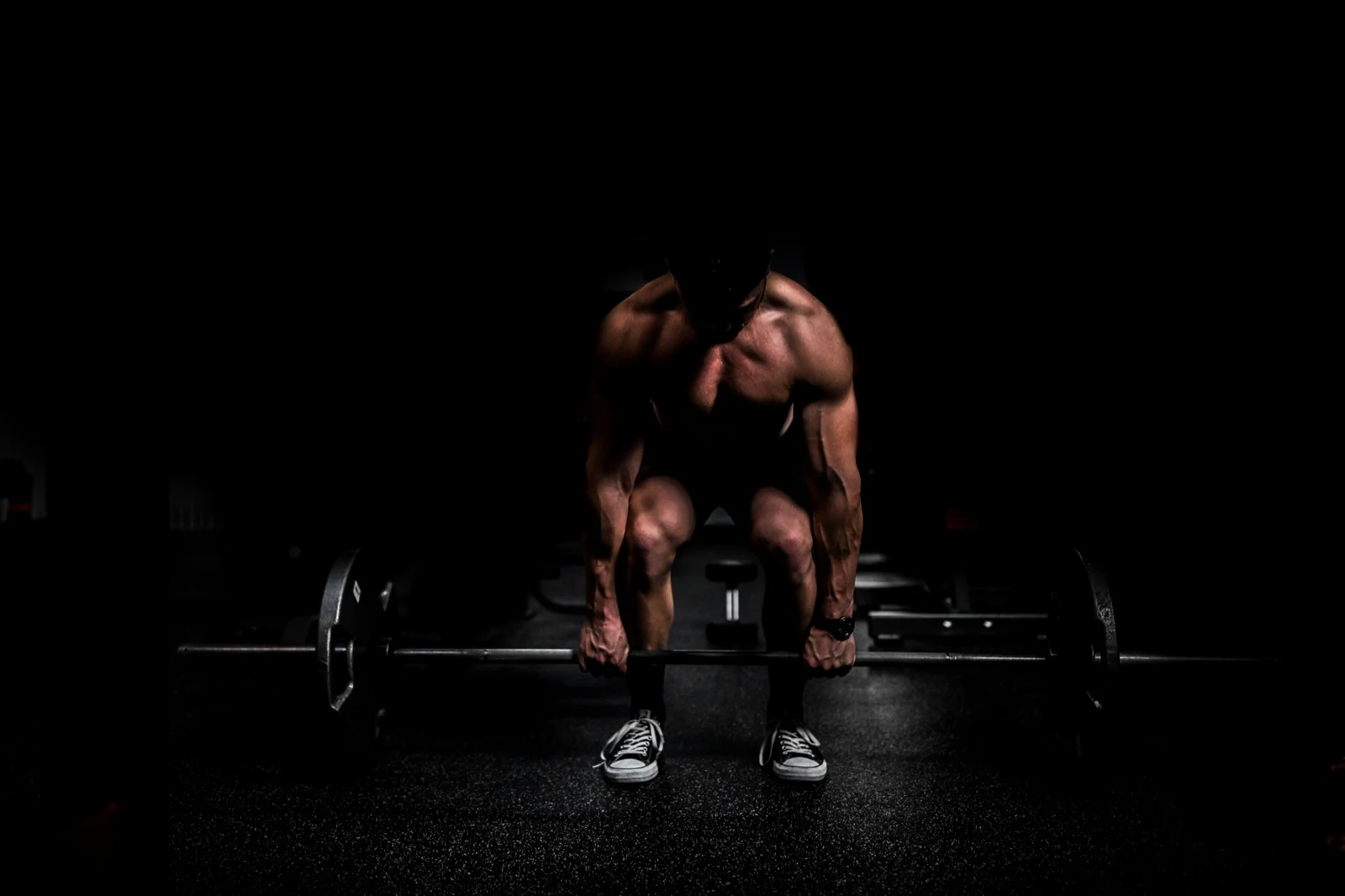 Lifter in a dark gym gripping a loaded barbell, about to start a deadlift